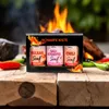 A gift box of spicy mustards is displayed in front of a campfire with chili peppers. Produktbild-Vorschau