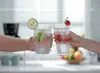 Two hands holding glasses of sparkling water with fruit garnishes, suggesting a refreshing beverage. Podgląd zdjęcia produktu