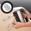 A person is holding a black and silver hand mixer with beaters attached. Produktbild-Vorschau