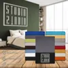 A stack of colorful bedding sheets is displayed in front of a bedroom scene with a bed and a wall graphic. Produktbild-Vorschau