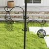 A black metal bird feeder station with two hanging feeders is shown in a grassy yard with stone steps and a house in the background. Voir les images du produit