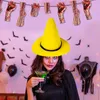 A woman in a yellow witch hat holds a green drink at a Halloween party. Produktbild-Vorschau