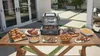 A table laden with food and an open electric grill, set up outdoors on a patio. Voir les images du produit