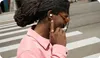 A person wearing earbuds and a pink shirt on a street crossing. Produktbild-Vorschau