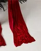 A close-up view of a red velvet Christmas bow draped over a white surface, with a hint of a Christmas tree branch at the top. Podgląd zdjęcia produktu