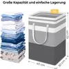 A stack of folded clothes next to a large fabric laundry basket with dimensions indicated. Produktbild-Vorschau