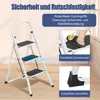 A white folding step stool with three steps, shown in a room with a wooden floor and a window in the background. The image includes close-up insets highlighting features like non-slip grips and feet, and a person's foot wearing a slipper on one of the step Produktbild-Vorschau
