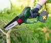A person wearing gloves is holding a cordless chainsaw and cutting a branch in an outdoor setting with lush green foliage in the background. Produktbild-Vorschau