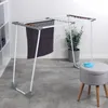 A laundry drying rack with a dark towel hanging on it, placed in a room with a shelf unit and a potted plant. Produktbild-Vorschau