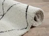A close-up view of a rolled-up shaggy rug with a diamond pattern. Produktbild-Vorschau