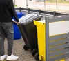 A person is pushing a black trash bin next to a yellow trash bin and a blue trash bin. Náhled obrázku produktu