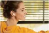 A woman wearing earbuds and a yellow hoodie, looking to the side. Anteprima dell’immagine prodotto