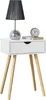 A white bedside table with a drawer, a lamp, and a clock on top, set against a white background. Náhled obrázku produktu