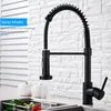 A black kitchen faucet with a pull-down sprayer is shown in use, with water flowing into a sink containing vegetables. Náhled obrázku produktu
