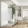 A modern bathroom with a glass-enclosed shower featuring a plant and pebbles, and a vanity area with shelves and a sink. Voir les images du produit