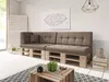 A modern living room with a sectional sofa made of wooden pallets and upholstered cushions, a coffee table, and decorative items. Produktbild-Vorschau
