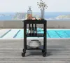 A black serving cart with bottles, glasses, and plates is placed on a wooden deck next to a swimming pool with a view of islands and the ocean. Anteprima dell’immagine prodotto