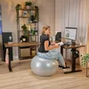 A woman is working at a standing desk while sitting on an exercise ball in a home office setting. Produktbild-Vorschau