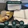A stack of checkered kitchen towels with a cup and cookies on a decorative tray. Produktbild-Vorschau