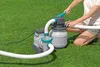 A person is kneeling on grass, operating a pool filter pump. Produktbild-Vorschau