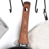 A close-up view of a frying pan handle hanging on a hook, with fabric items on either side. Produktbild-Vorschau