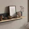 A wooden shelf mounted on a wall, decorated with various items including candles, a framed picture, and vases. Produktbild-Vorschau