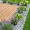Dalmatiner-Zierkieselsteine als Beetumrandung einer Holzterrasse mit blühenden Pflanzen Produktbild-Vorschau