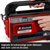 A close-up shot of a person's hands operating a red and black portable air compressor, with a digital display showing pressure readings. Voir les images du produit