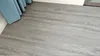 A close-up view of grey vinyl flooring with a wood grain texture, partially covered by a blue curtain. Anteprima dell’immagine prodotto
