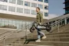 A man is walking up stairs outdoors, carrying a folded electric scooter. Produktbild-Vorschau