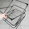A hand is shown adjusting a black metal drying rack with multiple tiers. Náhľad obrázku produktu