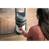 A woman is interacting with a tall, cylindrical air purifier. Podgląd zdjęcia produktu