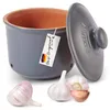 A ceramic garlic keeper with a lid, along with three garlic bulbs, is displayed against a white background. A tag with German text and the German flag colors is attached to the keeper. Produktbild-Vorschau