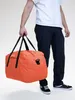 A person is holding an orange duffel bag. Náhľad obrázku produktu