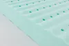 A close-up, angled view of a light green foam mattress topper with a wavy surface and small circular perforations. Produktbild-Vorschau
