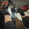 Two people wearing black gloves are holding and examining a black object, possibly a part of a device or tool. Produktbild-Vorschau