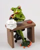 A figurine of a frog sitting at a desk with a laptop and papers. Produktbild-Vorschau
