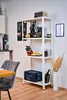 A white shelving unit with various items on it, including a coffee machine, books, kitchenware, and a crate of drinks, placed in a room with a chair and table in the foreground. Produktbild-Vorschau