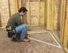 A man is kneeling on a wooden floor, working on a construction project. He is using a metal measuring tool. Náhled obrázku produktu