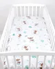 A white crib with a white crib sheet featuring a pattern of deer and trees. Produktbild-Vorschau