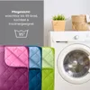 A quilted blanket in multiple colors is shown next to a washing machine, with text describing its care instructions. Produktbild-Vorschau