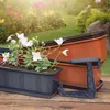 A collection of KADAX 'Oste' planters with white flowers, set in a garden environment. Podgląd zdjęcia produktu