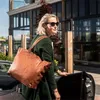 A woman is getting into a car with a large brown leather tote bag. Voir les images du produit