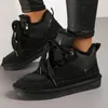 A pair of black winter sneakers worn by a person. Anteprima dell’immagine prodotto