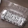 A clear plastic organizer box filled with neatly coiled cables and power adapters, placed on a wooden surface. Produktbild-Vorschau