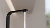 A close-up of a black kitchen faucet with water flowing out. Produktbild-Vorschau