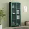 A green glass-door cabinet filled with decorative items, placed in a room with a plant and a framed picture on the wall. Podgląd zdjęcia produktu