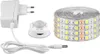 A white LED light strip kit with a power adapter and a motion sensor is laid out on a white background. Produktbild-Vorschau