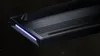 A close-up view of a black gaming keyboard with a purple LED light strip on the side, set against a dark, starry background. Produktbild-Vorschau