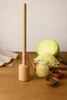 A wooden kraut pounder, a cut cabbage, shredded cabbage, and spices are arranged on a wooden table. Produktbild-Vorschau